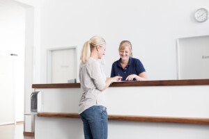 Praxisdame empfängt Kundin am Praxisklink-Empfangstresen