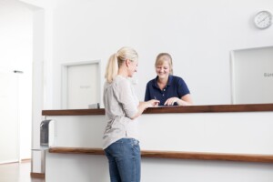Praxisdame empfängt Kundin am Praxisklink-Empfangstresen